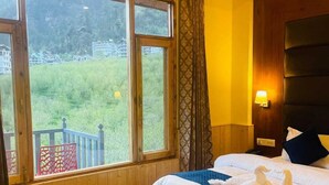 Ett hotellrum med ett stort fönster, trägolv, en säng med vita sängkläder och ett sängbord med en lampa.