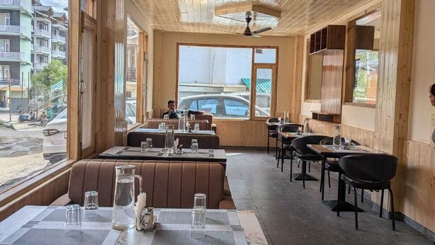 En restaurang med träpanel i tak och på väggarna, stora fönster och utsikt över gatan.