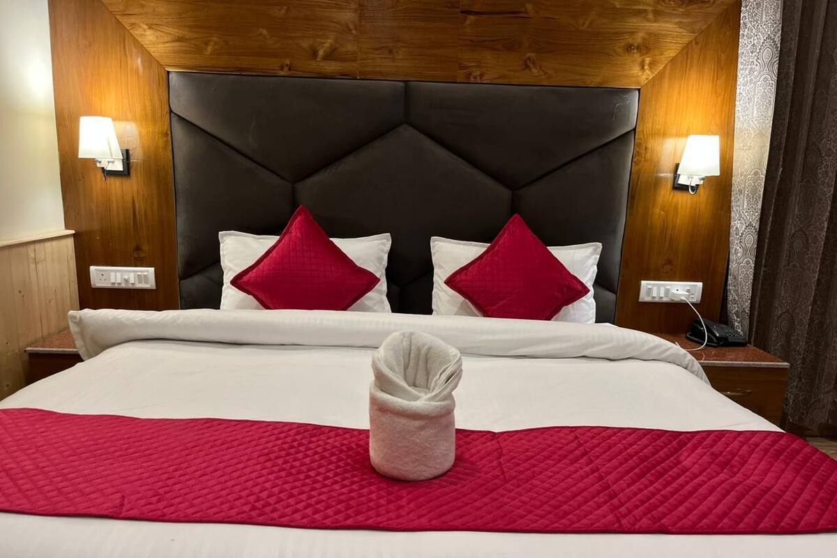 Quarto de hotel com uma cama grande, cabeceira de madeira, duas luminárias de cabeceira e um edredom acolchoado vermelho.