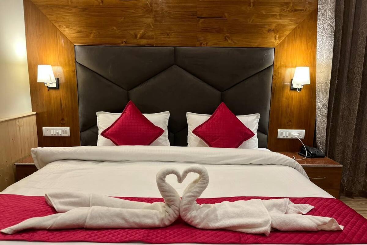 Quarto de hotel com uma cama grande, duas mesas de cabeceira e um painel de cabeceira de madeira.