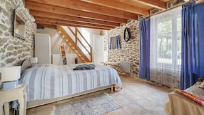 A bedroom with a bed, a desk, a chair, a stone wall, and a window with curtains. - Holiday Home 'Gite Renouard' with Private Garden, Wi-Fi and Air Conditioning (Saint-Cast-le-Guildo)