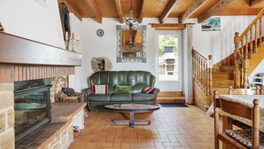 A cozy living room with a fireplace, a green leather sofa, a wooden dining table, and a staircase. - Holiday Home 'Gite Renouard' with Private Garden, Wi-Fi and Air Conditioning (Saint-Cast-le-Guildo)