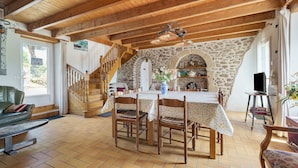 A dining area with a wooden table, chairs, and a stone wall. - Holiday Home 'Gite Renouard' with Private Garden, Wi-Fi and Air Conditioning (Saint-Cast-le-Guildo)