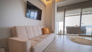 A modern living room with a sofa, a flat-screen TV mounted on the wall, and a large glass door leading to an outdoor area. - Althea Suites 4 by Rentals Pro - Nea Moudania Halkidiki (Nea Moudania)