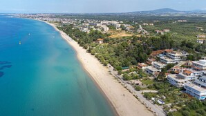 An aerial view of a coastal area with a beach, residential buildings, and a distant cityscape. - Althea Suites 4 by Rentals Pro - Nea Moudania Halkidiki (Nea Moudania)