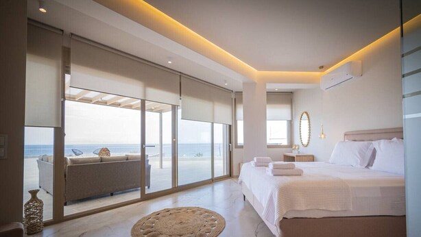 A bedroom with a large bed, a view of the sea, and a balcony with seating. - Althea Suites 4 by Rentals Pro - Nea Moudania Halkidiki (Nea Moudania)