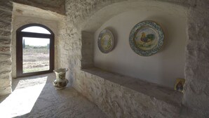 Un intérieur rustique avec un mur en pierre, une fenêtre, une étagère ornée d’assiettes décoratives et un vase.