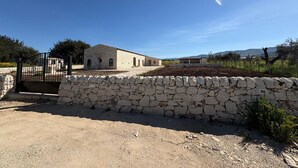 Un bâtiment en pierre doté d’une porte, entouré d’un mur en pierre et bordé d’un chemin de gravier.