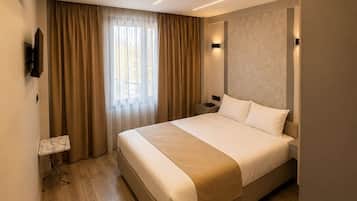 Ein modernes Hotelzimmer mit einem großen Bett, einem Nachttisch, einem am Wand montierten Fernseher und einem Fenster mit Vorhängen.