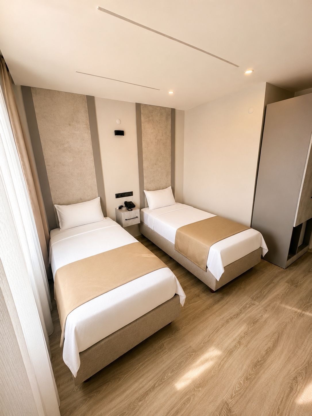 A hotel room with two beds, a bedside table, a small desk, and a wardrobe.