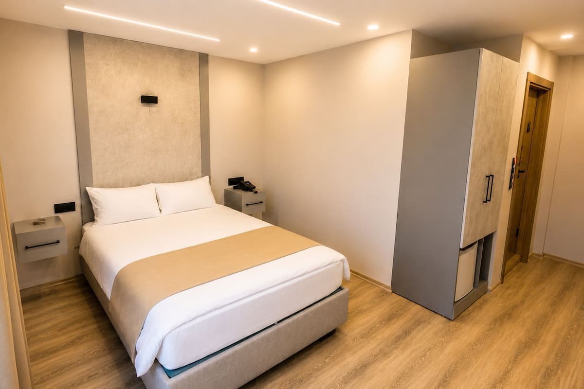 Ein modernes Hotelzimmer mit Bett, Nachttischen, einem Kleiderschrank und einer eingebauten Garderobe mit Spiegel.