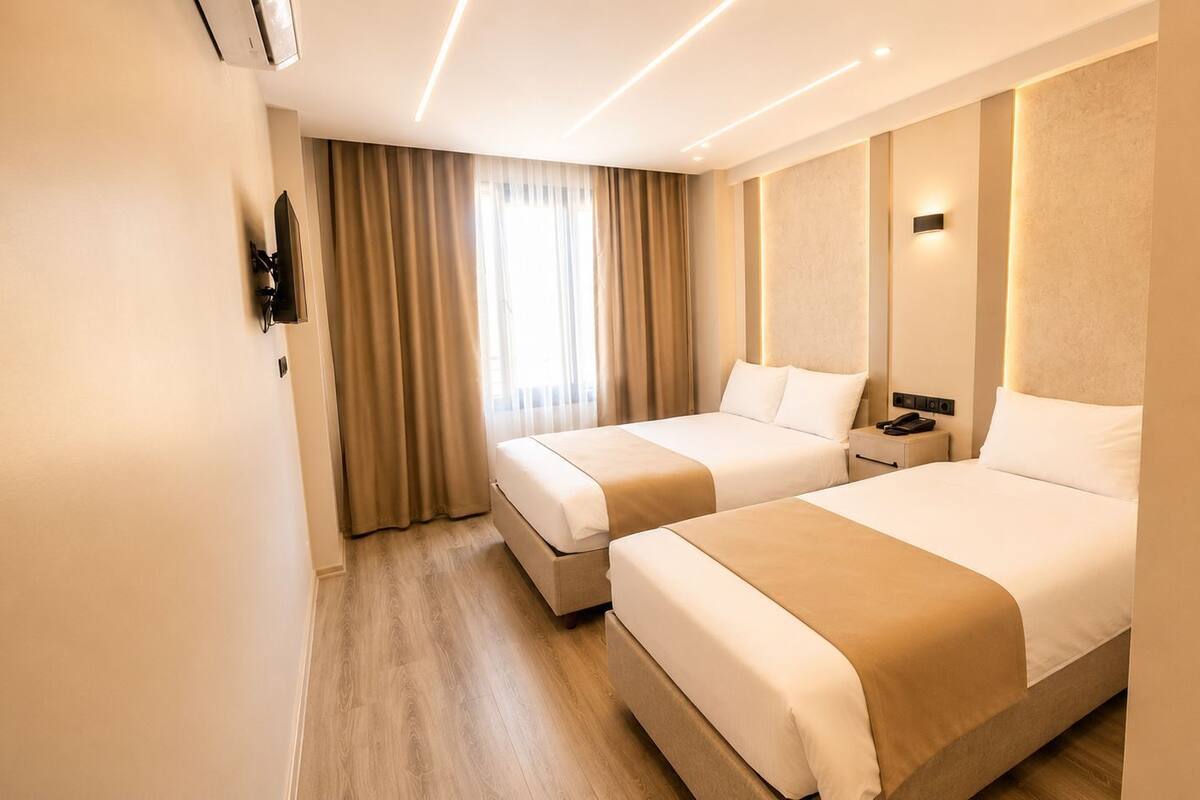 Ein Hotelzimmer mit zwei Betten, einem Nachttisch, einem an der Wand montierten Telefon und einem Fenster mit Vorhängen.