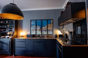 A modern kitchen with a central island, pendant lighting, and a cityscape artwork on the wall. - Stylish Montpellier Apartment for 4 (Montpellier)