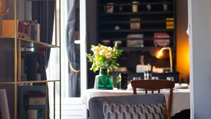 Ein Zimmer mit Bücherregal, Tisch mit Blumenvase und Stuhl.