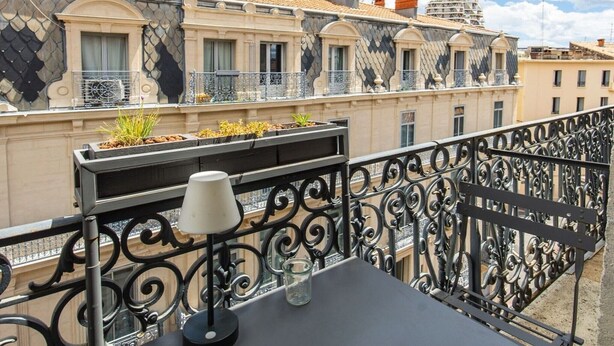 Ein Balkon mit schmiedeeisernen Geländern, einem kleinen Tisch mit Lampe und einem Blumentopf mit Pflanzen.