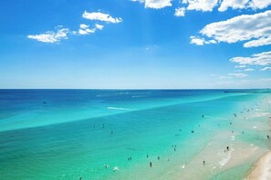 Ein Strand mit klarem türkisblauem Wasser, einer Seebrücke und badenden Menschen.