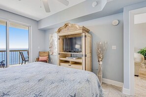 Een slaapkamer met een groot bed, een televisie op een houten kast, een balkon met uitzicht en een stoel.