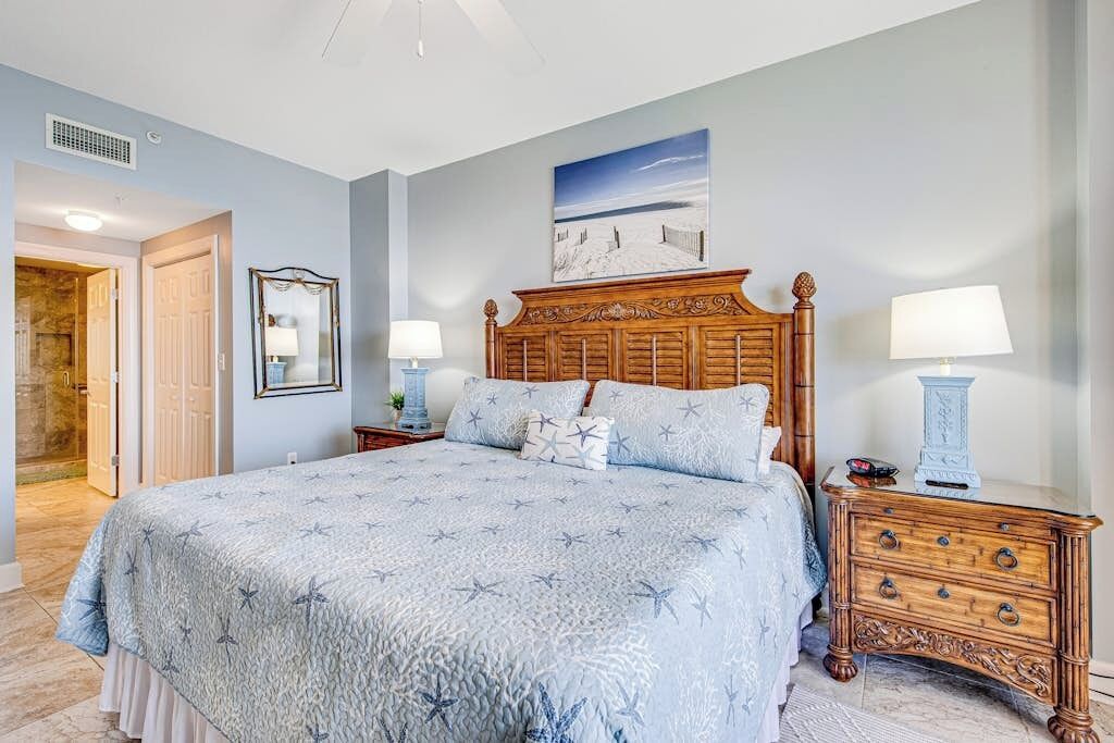 A bedroom with a large bed, two bedside tables with lamps, a wooden dresser, and a framed picture on the wall.