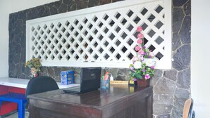 Un comptoir d’accueil avec un ordinateur portable, une chaise bleue, une cloison ajourée blanche et un vase avec des fleurs.