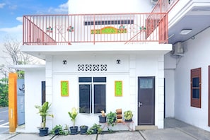 A two-story building with a balcony, potted plants, and a door with a small step leading to the entrance.