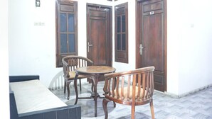 Une pièce comprenant un lit, une petite table et deux chaises. On y trouve trois portes en bois et une fenêtre avec des volets.