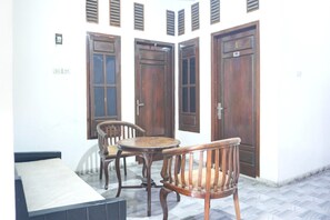 A room with a bed, a small table, and two chairs. There are three wooden doors and a window with shutters.