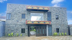 Un bâtiment moderne avec une façade en pierre, une grande entrée surmontée d’une arche décorative et une allée d’accès fermée par un portail.