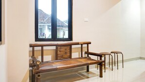Une pièce avec un banc en bois, deux tabourets, une fenêtre donnant sur des immeubles et un interrupteur sur le mur.