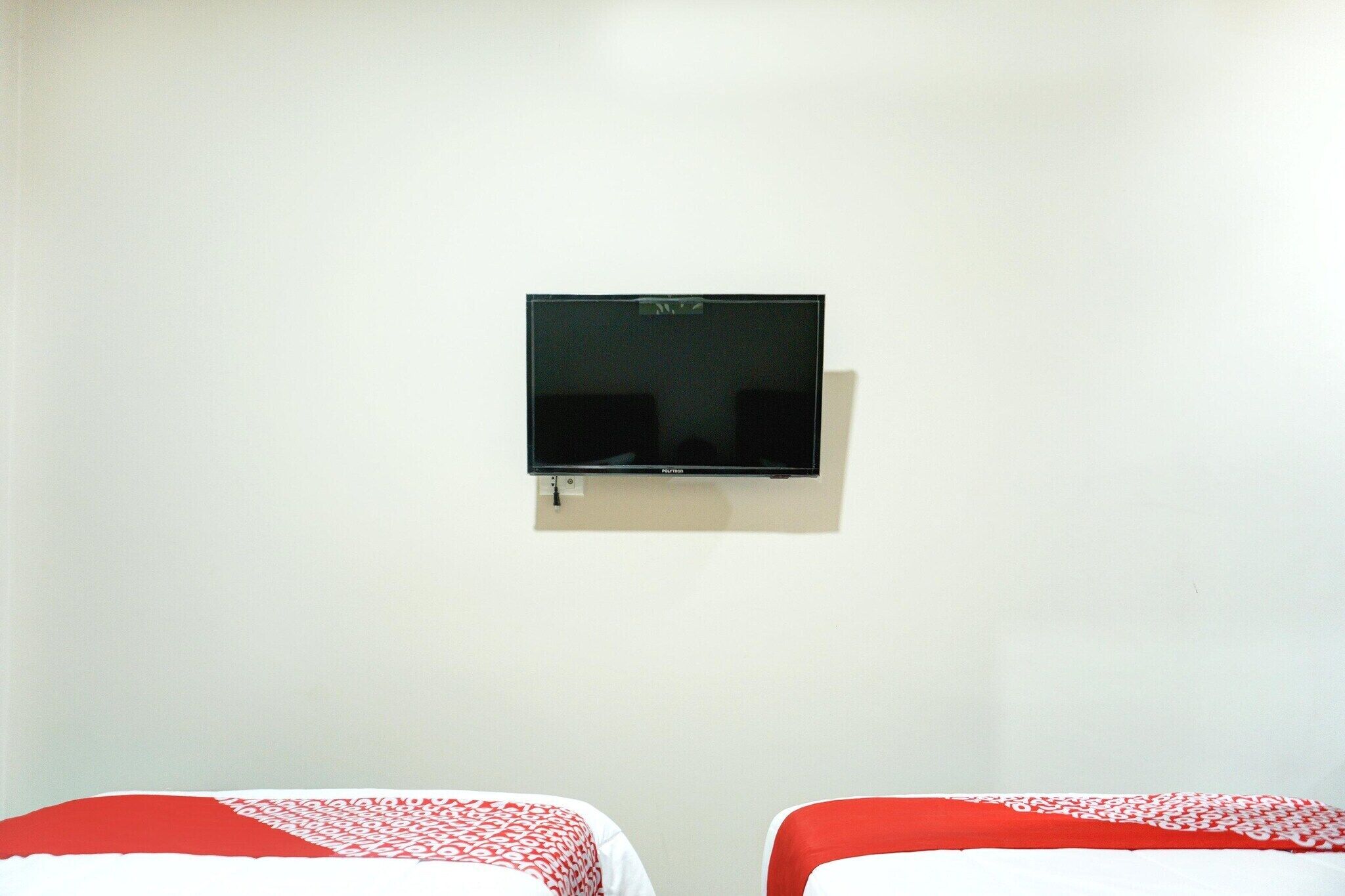 Une chambre avec deux lits, un téléviseur fixé au mur et un mur blanc uni.
