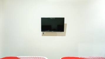 Une chambre avec deux lits, un téléviseur fixé au mur et un mur blanc uni.