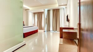 Una habitación de hotel con cama, tocador con espejo y un gran ventanal con cortinas.