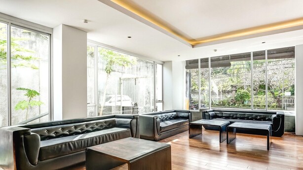 A modern lounge with leather sofas, wooden flooring, and large windows offering views of greenery.
