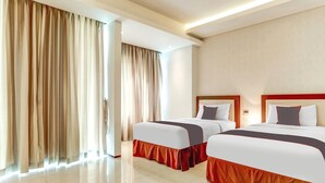 Een hotelkamer met twee bedden, een groot raam met gordijnen, een flatscreen-tv en een wandlamp.