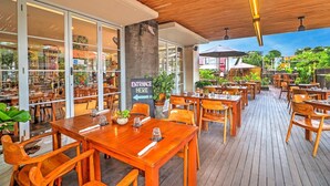 An outdoor restaurant with wooden tables and chairs, a concrete pillar, and a sign indicating the entrance. - Luxury Two Bedroom Villa with Pool and WiFi Access (Bali)