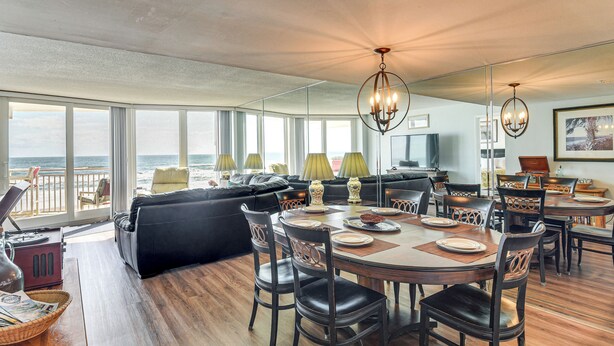Een ruime woonkamer met een groot raam met uitzicht op de oceaan, een eettafel gedekt voor vier personen, en een gezellige zithoek met een bank en fauteuils.