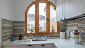 Une cuisine avec une fenêtre à cadre en bois, un évier blanc et une plante en pot posée sur le plan de travail.