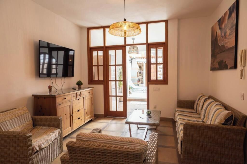 Ein Wohnzimmer mit Rattanmöbeln, einem Flachbildfernseher, einem Holzschrank und einem großen Fenster.