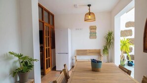 Un coin repas comprenant une table en bois, des chaises, un banc, un réfrigérateur et des plantes en pot.