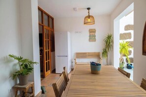 A dining area with a wooden table, chairs, a bench, a refrigerator, and potted plants. - Casa Mari. (Agaete)