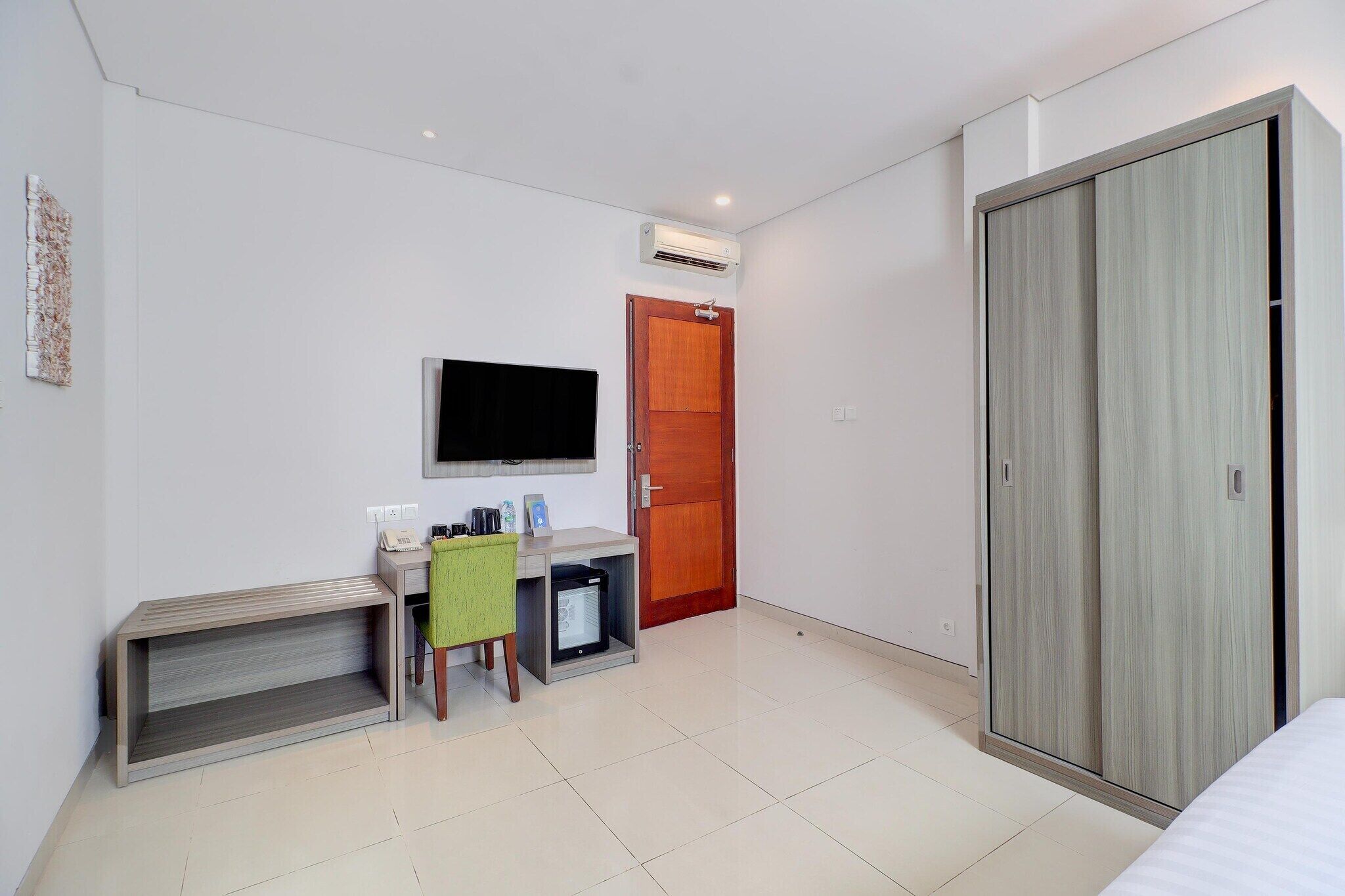 A hotel room with a bed, a desk with a chair, a television, a wardrobe, and a door.