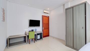 A hotel room with a bed, a desk with a chair, a television, a wardrobe, and a door.