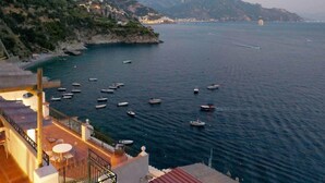 Una vista sulla costa con barche sull'acqua, montagne sullo sfondo e un edificio con posti a sedere all'aperto.