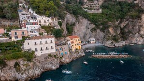 Un villaggio costiero con edifici costruiti a ridosso della scogliera, un porto turistico con imbarcazioni e un terreno roccioso.