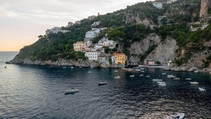 Une ville côtière avec des bâtiments perchés sur une falaise, des bateaux sur l’eau et un ciel dégagé.
