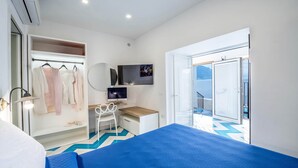 Une chambre d’hôtel moderne équipée d’un lit, d’un bureau, d’une chaise, d’une télévision, d’une armoire et d’un balcon avec vue.