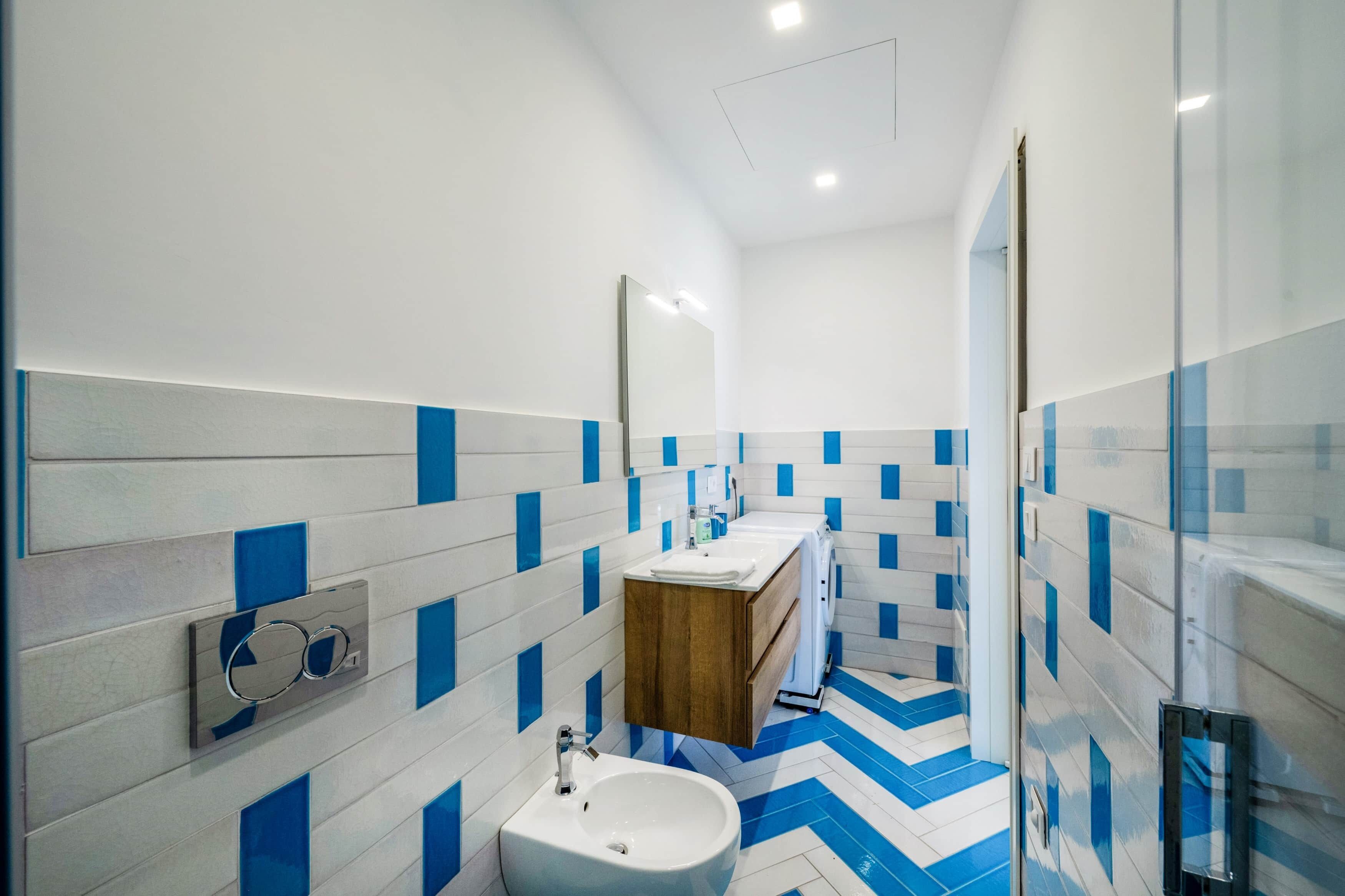 Un baño moderno con piso de azulejos blancos y azules, un mueble de tocador de madera, un lavamanos blanco y un espejo.