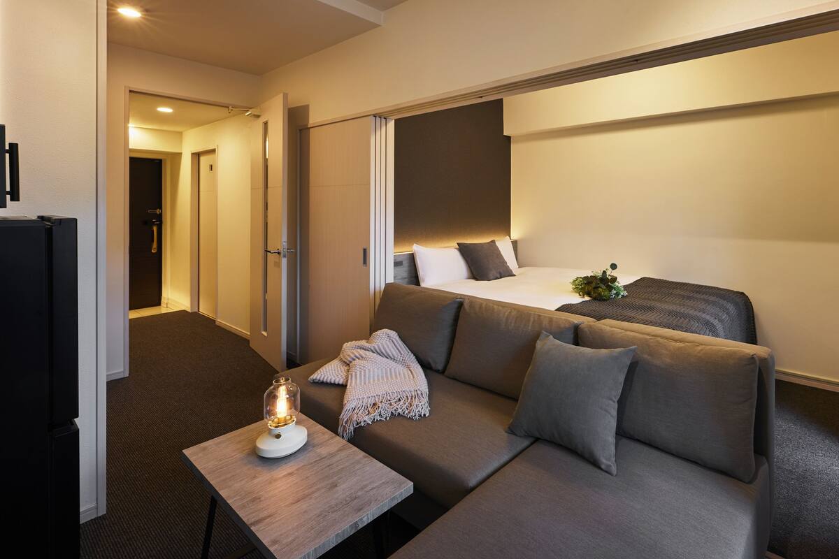 Ein Hotelzimmer mit einer Couch, einem kleinen Tisch mit Lampe, einem Bett und einer Tür zu einem weiteren Raum.