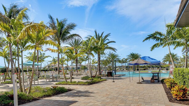 A resort pool area with palm trees, lounge chairs, and a covered seating area. - New Home in Verdana Village w/ Resort Amenities! (Estero)