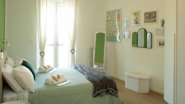 Een slaapkamer met een bed, nachtkastje, raam met gordijnen, een wandspiegel en een radiator.