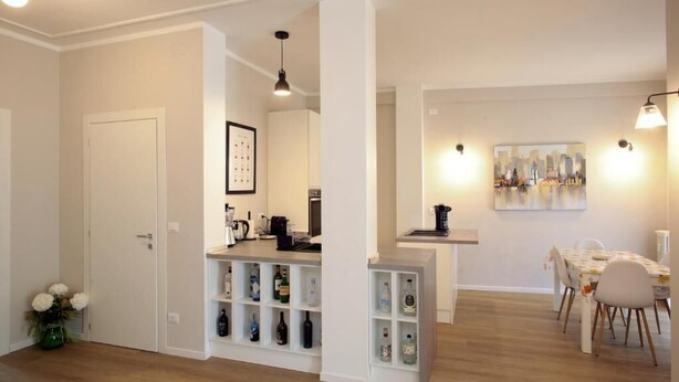 A modern kitchen with built-in shelves, a dining area with a table and chairs, and a cityscape painting on the wall. - Federica Flat - Metro Monte Grappa (Turin)